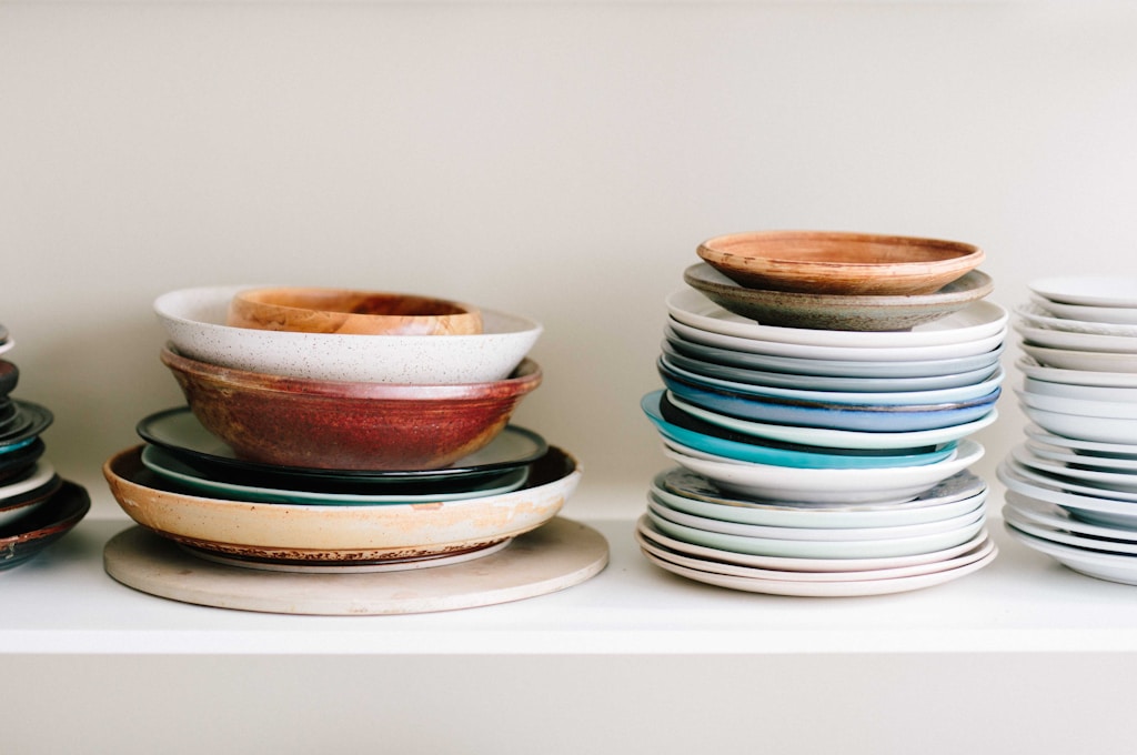 Stacked handcrafted ceramic plates and bowls on an open kitchen shelf