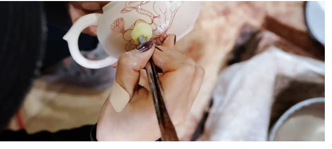A craftsperson hand-painting a floral glaze design onto a porcelain cup