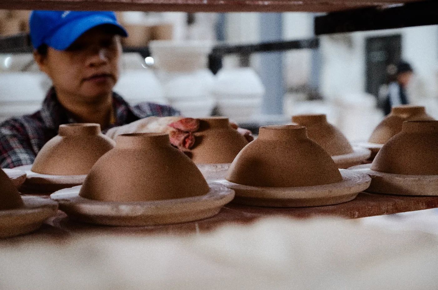 An artisan tending rows of unfired clay bowls drying in a workshop