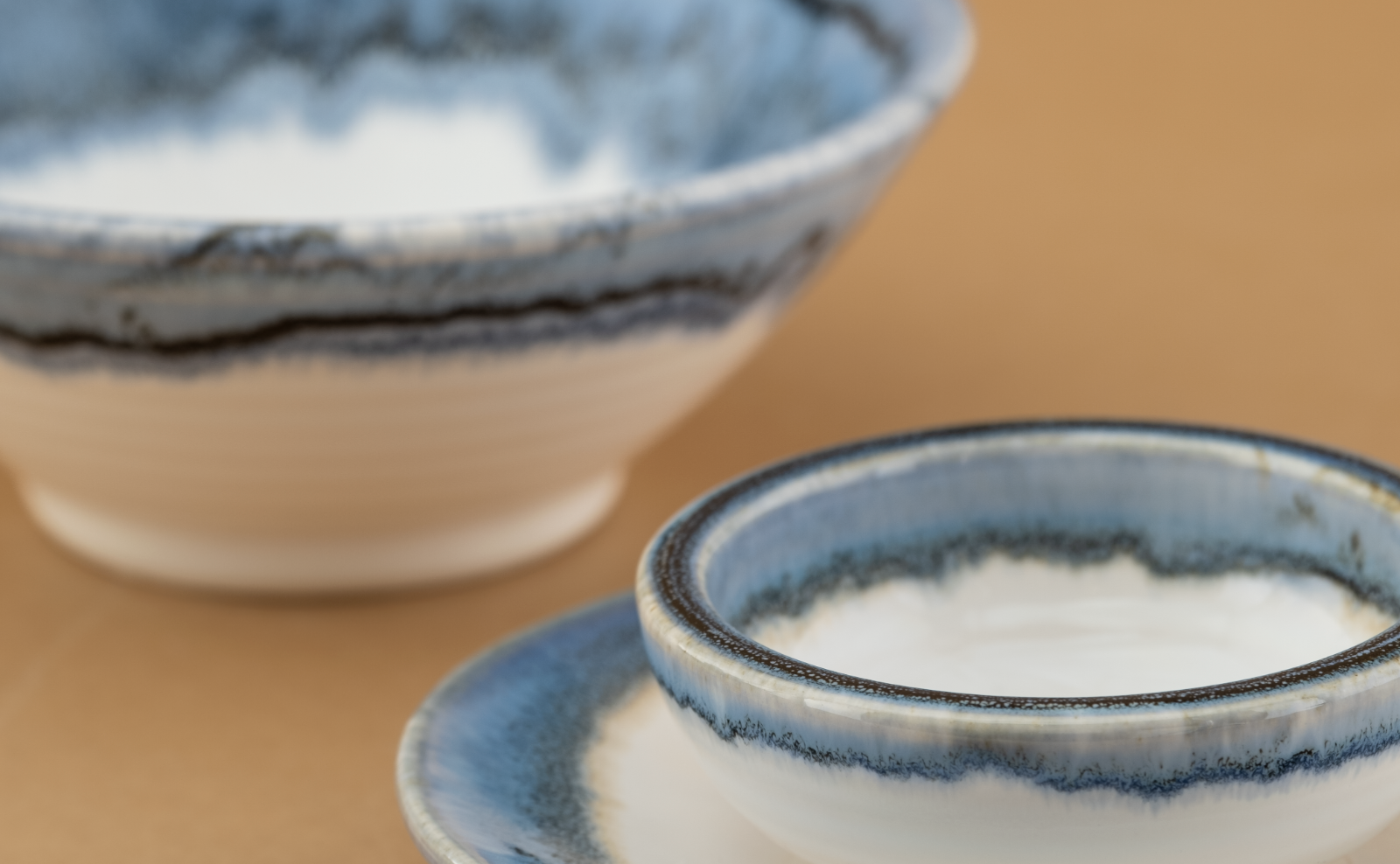 Frosted Wave cup and bowl in white porcelain with an ice-blue glaze breaking into dark feathered veins