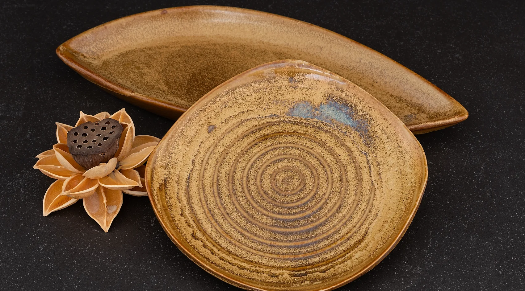 Harvest Sun coupe plate and leaf-shaped dish on dark slate, amber glaze with concentric throwing rings