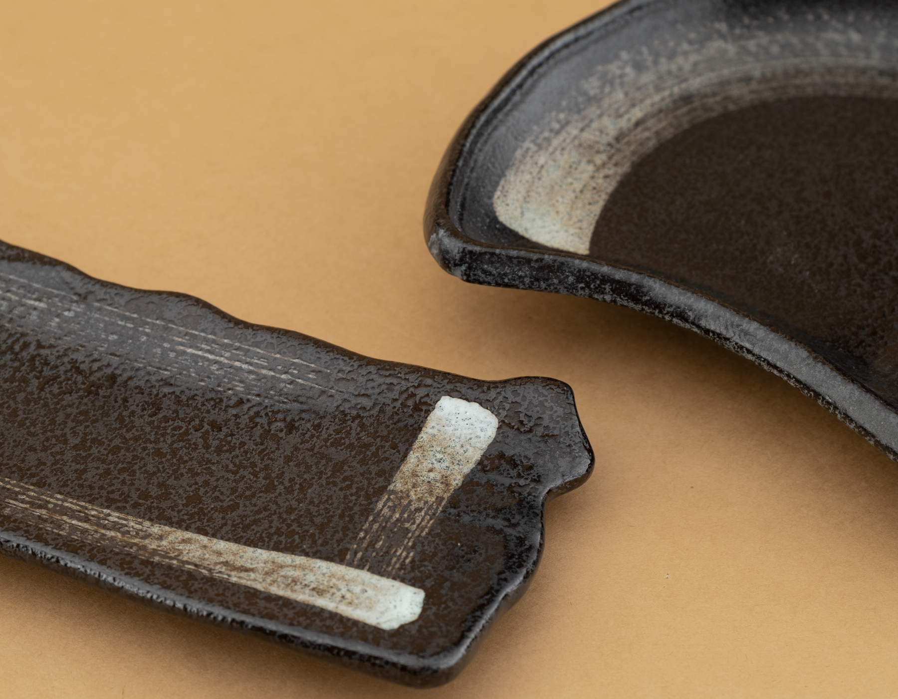 Close-up of two Shadow Stone pieces, near-black glaze wiped back to a brushed stone-grey swipe