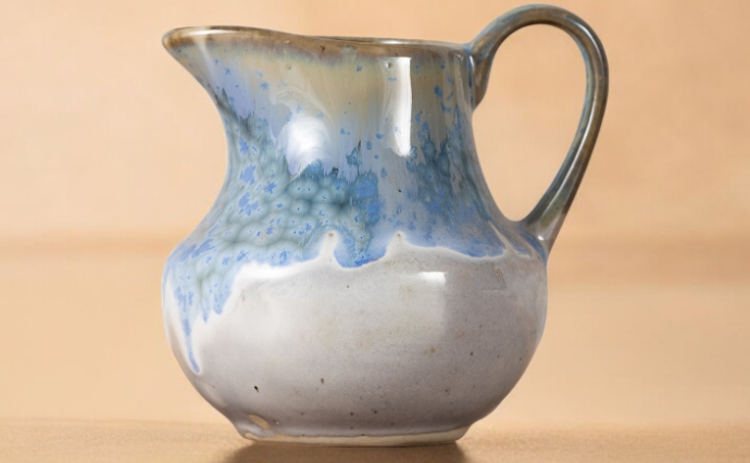 A Starry Seas jug on a warm wooden surface, showing the pale blue crystalline speckle running down into the oatmeal glaze