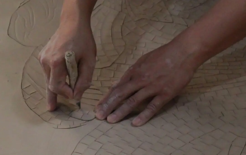 Hands cutting and laying ceramic mosaic pieces by hand